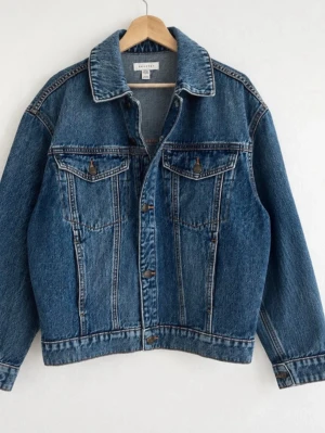 Ny Klassisk blå jeansjacka från Topshop - Snygg blå jeansjacka från Topshop i klassisk modell med två bröstfickor med lock och knappar framtill. Jackan har en avslappnad passform och tidlös design som passar till det mesta. Perfekt att slänga över en hoodie eller t-shirt.
