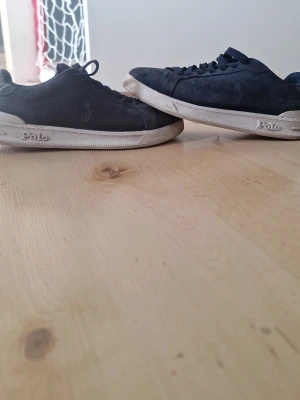 Typ helt nya Mörkblå Polo Ralph Lauren sneakers - Snygga mörkblå sneakers från Polo Ralph Lauren med ovandel i mocka och klassisk låg siluett. Skorna har vita sulor med Polo-logga på sidan och rutigt innerfoder. Perfekta för en stilren och avslappnad look.
