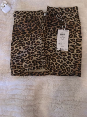 Leopardmönstrad kortkjol från Name It - Säljer en snygg kortkjol från Name It med leopardmönster i bruna och svarta toner. Kjolen har klassisk jeanskjolsdesign med knapp och dragkedja framtill samt fickor. Perfekt för dig som vill sticka ut med en trendig look.💗💓🫰🏻