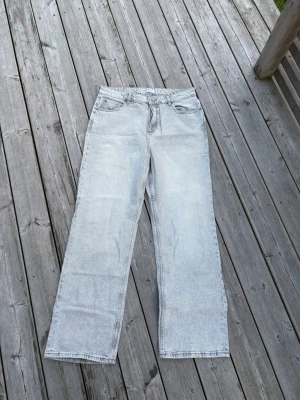 Ljusgråa raka jeans - Säljer ett par ljusgråa jeans med rak passform och hög midja. Jeansen har klassisk femficksdesign och är tillverkade i denim. Perfekta för dig som gillar en avslappnad och trendig stil.