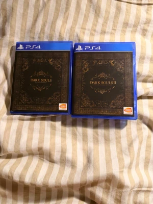Dark Souls 1 och 2 till PS4-PS5 - Säljer Dark Souls, Dark Souls II: Scholar of the First Si till PS4. Alla spel har snygga svarta fodral med gulddetaljer och blå plastomslag. Perfekt för dig som gillar utmanande action-RPG och vill ha  Alla DLC inkluderat