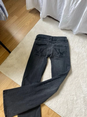 Svarta lågmidjade bootcut jeans med broderade fickor - Säljer ett par svarta bootcut jeans med snygga broderade detaljer på bakfickorna, de är sydda till lågmidjade och är därför lite tightare i låren. Jeansen har klassisk femficksmodell, bälteshällor och stängs med knapp och dragkedja. Materialet är mjukt denim som sitter skönt hela dagen. 