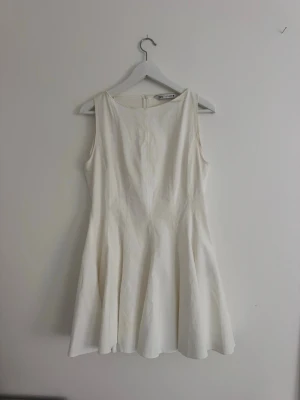 Vit miniklänning från Zara - Säljer en stilren vit kortklänning med ärmlös design och rund hals. Klänningen har en lätt utställd kjol och dragkedja i ryggen. Perfekt för sommarens alla tillfällen! Andänd endast en gång på studenten. 