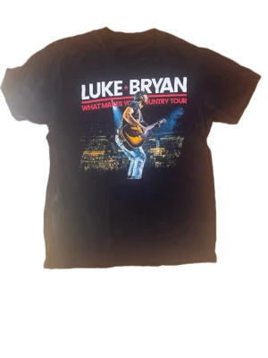 Svart Luke Bryan tour t-shirt SIZE L - Fint skick  Storlek saknas på taggen men motsvarar L baserat på måtten: • Längd: 74.5 cm • Pit to pit: 51 cm • Axlar: 46 cm • Ärm: 22 cm • Hem width: 55 cm.                                  Säljer en svart t-shirt med tryck från Luke Bryans 'What Makes You Country Tour'. Framsidan har ett stort motiv av Luke Bryan med gitarr på scen och text i vitt och rött. Perfekt för dig som gillar musik och vill sticka ut med en cool bandtröja.