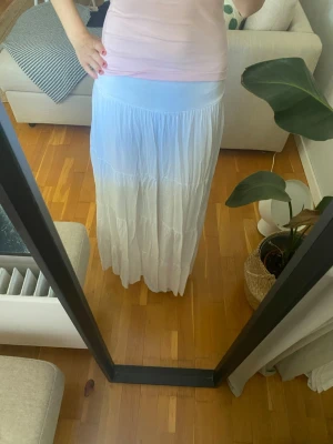 Vit långkjol med volang - Säljer en luftig vit långkjol med volangdetaljer. Kjolen är lång och går ner till fötterna på mig som är 166cm. Tillhörande skärp kommer med.💞
