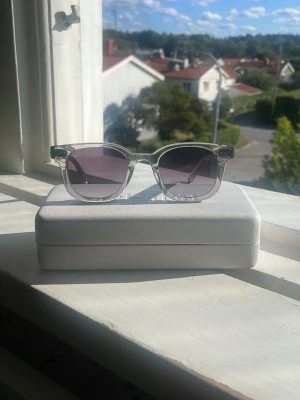 Chimi solglasögon gråa 02 - Snygga solglasögon med transparent båge och fyrkantig form. Glasen har en mörkgrå ton som ger en cool look. Perfekta för soliga dagar och passar till de flesta outfits.