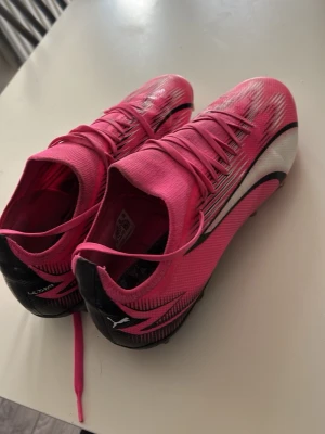 Puma Ultra rosa fotbollsskor - Säljer ett par grymma Puma Ultra fotbollsskor i en riktigt snygg rosa färg med svarta och vita detaljer. Skorna har låg profil, snörning och mönstrad ovandel för bra bollkontroll. Perfekta för dig som vill sticka ut på planen!. Finns inte sula på de!