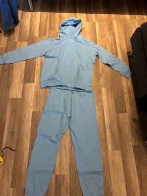 Ljusblått loungewear-set från Ellos - Mysigt loungewear-set från Ellos i ljusblå bomull. Setet består av en hoodie med känguruficka och matchande byxor med resår i midjan och benslut. Perfekt för chill dagar hemma eller när du vill vara extra bekväm.