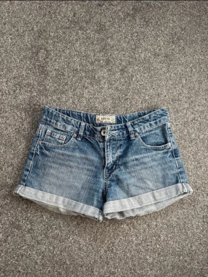 Blå jeansshorts från Donna by Dixie - Säljer ett par klassiska blå jeansshorts från Donna by Dixie i 100% bomull. Shortsen har uppvikta benslut, två bakfickor och bälteshällor. Perfekta för varma dagar och enkel att matcha med olika toppar.
