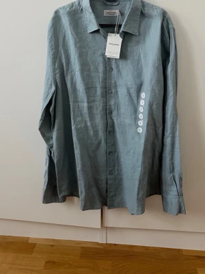 Ljusblå linneskjorta från Dressmann - Säljer en stilren ljusblå skjorta från Dressmann i 100% linne. Skjortan har klassisk krage, långa ärmar och knappar framtill. Perfekt för dig som gillar en avslappnad men ändå snygg look.