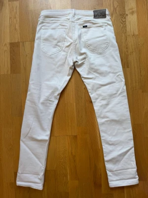 W33 L36 Vita jeans Lee LUKE - Säljer ett par vita jeans från Lee med klassisk femficksmodell och raka ben. Jeansen har Lee-logga på bakfickan och patch i midjan. Materialet är mjukt och slitstarkt denim i bomull. Perfekta för dig som vill ha en clean och stilren look.