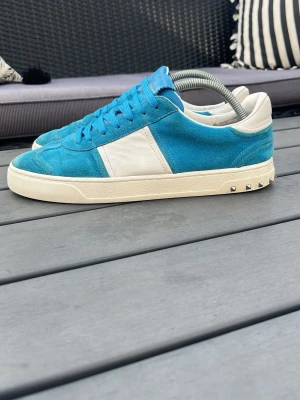 Valentino flycrew - Snygga sneakers i blå mocka och vitt läder från Valentino. Skorna har blå snörning, vit sula och coola nitar på hälen. Perfekta för dig som vill sticka ut med en unik färgkombination och exklusiv känsla. skorna är i fint skick och inga nitar saknas storleken är 40 men skulle säga att de passar lite mer som 41 har du frågor om skickat eller nåt annat är det bara att höra av dig jag tar det jättegärna byten också