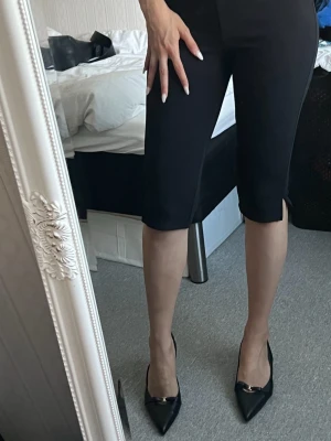 Capribyxor storlek m (oanvänd) - Säljer ett par svarta capris med snygg slits vid benslutet. Byxorna är tillverkade i ett mjukt, vävt material som ger en clean look. Perfekta till en stilren outfit. Mjuk och stilren! Ser exklusiva ut. I storlek medium!🥰 de säljs ej längre.