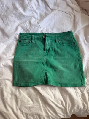 Grön kort jeanskjol med fickor - Snygg grön kort jeanskjol med klassiska fem fickor och knappstängning framtill. Kjolen har en rak passform och är perfekt för dig som vill ha en enkel men färgstark look. Passar till både sneakers och boots.