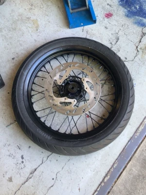 Sm däck/fälj fram - Säljer ett svart motorcykeldäck med tillhörande fälg och bromsskiva. Däcket har sportigt mönster och fälgen är ekrad i metall. Perfekt för dig som behöver reservdel till din hoj.