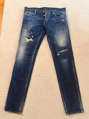 dsquared2  - Säljer ett par blå skinny jeans med slitningar och hål på låret och knät. Jeansen har en tvättad look med ljusare partier och klassisk femficksmodell. Passar dig som gillar en trendig och avslappnad stil.
