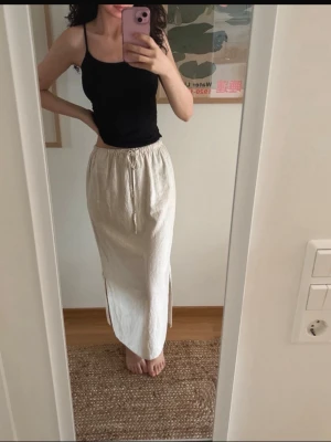 Kjol från SoyaConcept - Säljer en beige långkjol i linne och viskos med snörning i midjan och slits på sidan. Kjolen har en avslappnad passform och är perfekt för varma dagar. Enkel och stilren design som är lätt att matcha med olika toppar. Helt ny. Prislapp kvar. Köpt för 599 kr. Aldrig använd förutom när den testats för att fotas. Felstämplad med strl XXL, men är egentligen en XS-S. 