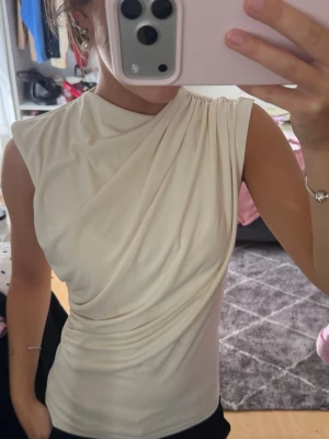 Vit draperad ärmlös topp - Säljer en beige/vit topp från Zara som har en draperad design. Använd ett fåtal gånger.
