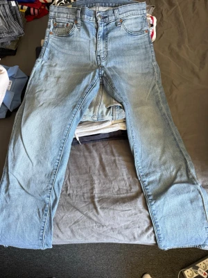 Ljusblå raka jeans från Levi's - Säljer ett par ljusblå jeans från Levi's med klassisk femficksmodell och raka ben. Jeansen har tydliga kontrastsömmar, läderpatch bak i midjan och den ikoniska röda Levi's-taggen på bakfickan. Perfekta för en avslappnad och trendig look.
