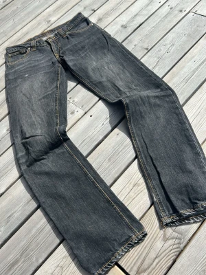 Svarta raka jeans med slitningar - Säljer ett par svarta jeans med raka ben och snygga slitningar. Jeansen har klassisk femficksmodell, kontrastsömmar i gult och en avslappnad passform. Perfekta för en casual look och tillverkade i slitstark denim.w28 L32