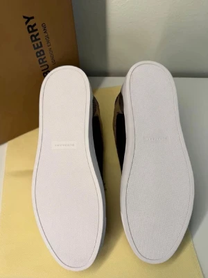Berry sneakers - Snygga sneakers från Burberry med klassiskt svartvitt rutmönster och vita sulor. Skorna har svarta detaljer och låg profil. Perfekta för dig som vill ha en stilren och trendig look med exklusiv känsla. Materialet är en mix av textil och mocka.
