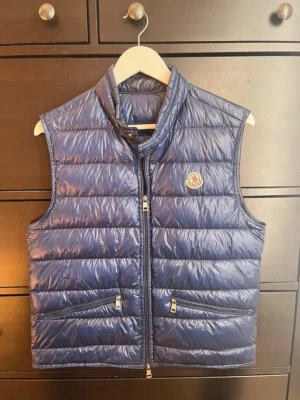 Moncler Gui väst - Tja. Säljer nu denna sjukt snygga och eftertraktade Moncler västen i den populära modellen Gui. Den är i jättefint skick och nästan som ny. Storlek 2 vilket motsvarar S/M(liten i storleken). Jättefin blå färg. Köpt på Haiendo för 3800kr och KVITTO finns. Nypris ligger runt 9000kr. Hör av er vid frågor/bilder eller funderingar👌🔥