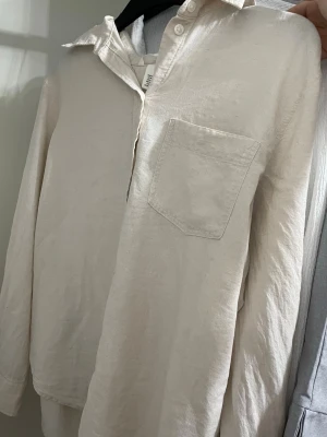 Beige linneskjorta med bröstficka - Säljer en stilren beige skjorta i linnemix med klassisk krage och bröstficka. Skjortan har lång ärm och knappar upptill, perfekt för en avslappnad men snygg look.