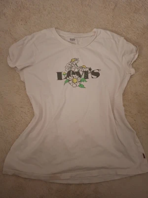 Vit Levi's t-shirt med blommor - Vit t-shirt från Levi's med tryck av blommor och logga på bröstet. Klassisk rund hals och korta ärmar. Perfekt för en avslappnad och trendig stil.