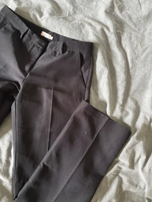 Svarta kostymbyxor från Nelly - Snygga svarta kostymbyxor från Nelly i rak modell. Byxorna har diskreta fickor och hällor för skärp. Perfekta till en stilren look och passar till många olika outfits. Materialet känns mjukt och följsamt. De har en medelhög midja på 22 cm med relativt långa i ben, Innerbenet är 82 cm och midjemått rakt över är 38 cm. 