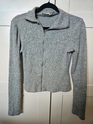 Top Lager 157 xs - Grå ribbad kofta från Lager 157, XS  Gråmelerad ribbad kofta från 157 i storlek XS. Tröjan har lång ärm, hög krage och hel dragkedja framtill. Materialet är stickat och känns mjukt och skönt. Perfekt för lager-på-lager och enkel att matcha med det mesta.  Kan även hämtas I Partille  E1