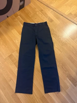 Mörkblå Dickies 874 chinos - Säljer ett par klassiska mörkblå Dickies 874 Original Fit chinos. Byxorna har rak passform, bälteshällor och är tillverkade i slitstarkt material som är en blandning av polyester och bomull. Perfekta för en clean och stilren look.