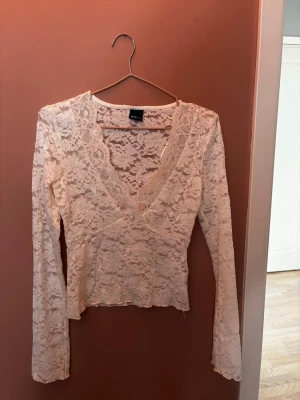Beige spetsblus med v-ringning - Säljer en beige långärmad blus i spets med v-ringad omlottfront. Blusen är genombruten med fina spetsdetaljer och har en feminin och elegant look. Perfekt att styla med jeans eller kjol för en trendig outfit.