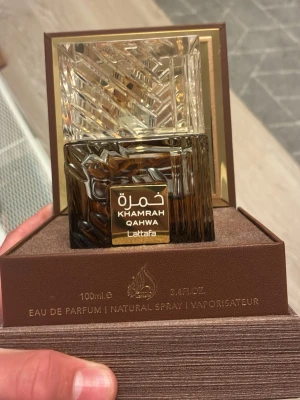 Khamrah Qahwa Eau de Parfum 100ml - Exklusiv parfym från Lattafa, Khamrah Qahwa, i en elegant fyrkantig flaska med guld- och bruna detaljer. Flaskan har ett unikt mönstrat lock i transparent material och rymmer 100 ml Eau de Parfum. Perfekt för dig som gillar lyxiga och orientaliska dofter. Denna perfym har knappast andvänts för den passade inte min smak.
