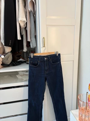 Mörkblå raka jeans med medelhög midja - Säljer ett par mörkblå jeans med raka ben och hög midja. Klassisk femficksmodell med knapp och dragkedja framtill. Jeansen har en tidlös look och passar perfekt till crop tops eller hoodies. Materialet är stretchigt denim som sitter snyggt och bekvämt.