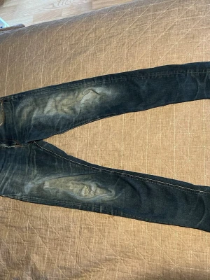 Mörkblå slim fit jeans med slitningar - Säljer ett par mörkblå slim fit jeans med snygga slitningar och tvättade detaljer på låren och knäna. Jeansen har klassisk femficksdesign och kontrastsömmar. Materialet är denim i bomull med lite stretch för skön passform.