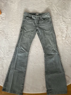 Ljusgrå bootcut jeans - Snygga ljusgrå jeans med bootcut passform och klassiska fem fickor. Jeansen har låg midja och subtila slitningar för en avslappnad look. Tillverkade i denim med lätt stretch för extra komfort.