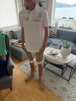 Gaastra Polo - Vit kortärmad skjorta med knappar och tryckdetaljer på bröstet och nacken. Skjortan har en klassisk krage som kan bäras uppvikt och är tillverkad i ett mjukt bomullsmaterial. Perfekt för en avslappnad och stilren look.
