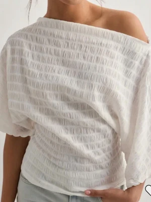 Vitt set med offshoulder topp och byxa - Snyggt vitt set med offshoulder topp och matchande byxa i lätt, strukturerat tyg. Toppen har lös passform och korta ärmar, medan byxorna är raka och luftiga. Perfekt för en trendig och avslappnad look. Slutsåld från Nelly i jättefint skick och man får med både byxa och tröja! Storlek xss men  stretchiga material