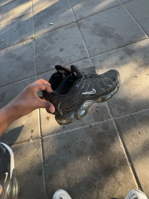 Svarta Nike sneakers med vita detaljer - Säljer ett par svarta Nike sneakers med vita prickar och detaljer. Skorna har en sportig design med synlig dämpning i sulan och klassisk Nike-logga på sidan. Perfekta för dig som gillar streetwear och vill ha något bekvämt och snyggt till vardags.