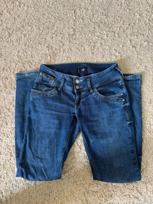 Blå jeans från LTB med raka ben - Snygga blå jeans från LTB med klassisk femficksdesign, raka ben och dubbla knappar i midjan. Jeansen har tydliga sömmar och slitningar för en trendig look. Perfekta för dig som gillar en avslappnad men stilren stil. W28 L30