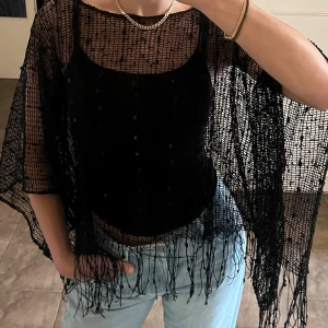 Svart virkad ponchotopp / poncho med fransar & paljetter (Y2K / Boho) - Superfin svart nätstickad/virkad poncho med snygga fransar nertill och diskreta små paljetter som ger ett fint lyster! Perfekt att styla över ett linne för en snygg lager-på-lager-look eller till festen/festivalen. Går även att ha som cover up till strand/pool.   Storlek ONESIZE, passar de flesta från XS-L beroende på vad man vill ha för passform. (Har vanligtvis S) 
