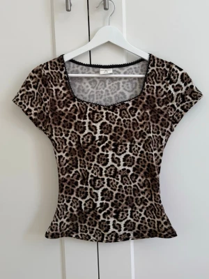 Leopardmönstrad topp med spetskant - Snygg leopardmönstrad topp med korta ärmar och svart spetskant runt den fyrkantiga ringningen. Figurnära passform som framhäver siluetten. Köpt på Ullared och aldrig använd💗