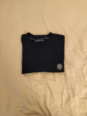 Svart t-shirt från Stone Island - Snygg svart t-shirt från Stone Island med klassisk rund hals och ikonisk logopatch på bröstet. Tillverkad i mjuk bomull för skön känsla och stilren look. Perfekt till jeans eller shorts för en clean outfit.