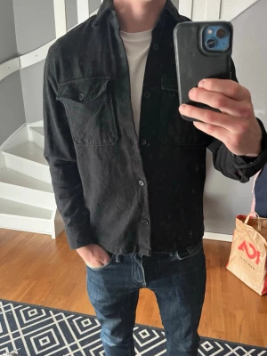 Svart overshirt med bröstfickor - Säljer en svart overshirt från Jack and Jones i väldigt bra skick. Perfekt att bära över en t-shirt. Storleken är S, hör av er vid frågor!