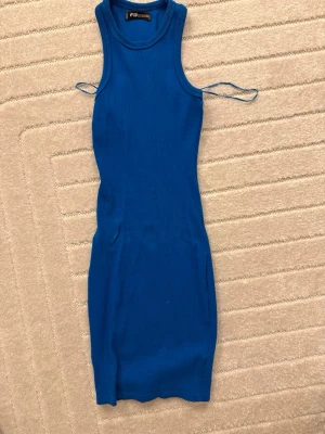 Blå ribbad kort klänning - Snygg blå ribbad klänning i kort modell med ärmlös design och rund hals. Klänningen har en kroppsnära passform och tunna axelband som ger en modern look. Perfekt för dig som vill ha en enkel men trendig outfit.