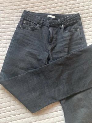 Svarta bootcut jeans och medel höga midjan - Snygga svarta jeans med bootcut passform och hög midja. Klassisk femficksmodell med bälteshällor och dragkedjegylf. Jeansen är i ett mjukt denimtyg som passar perfekt till en avslappnad stil. Andvänt 1 gång och är i bra skick.
