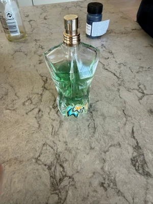 Jean Paul Gaultier parodies 80% - Unik parfymflaska i glas formad som en manlig överkropp med grön färg i botten och detaljer i blått och gult. Flaskan har guldfärgad spraykork och är en cool inredningsdetalj för badrumshyllan. 80% av perfymer kvar! 