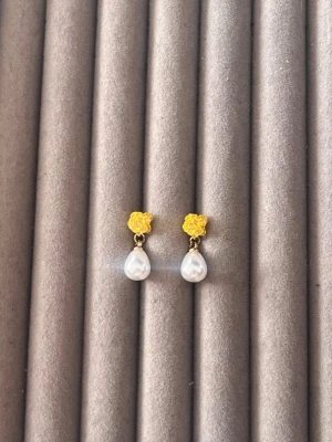 Guldörhängen med ros och pärldroppe - Snygga örhängen med guldfärgade rosor som fäste och droppformade vita pärlor som hänger ned. Perfekt för dig som gillar en söt och elegant stil. Stiftmodell i metall och pärlimitation.