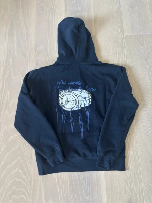 Mörkblå hoodie med tryck och  - Säljer en mörkblå hoodie med stor ficka framtill och huva med dragsko. På ryggen finns ett coolt tryck med en klocka och texten 'Who cares I'm already late'. Perfekt för dig som gillar streetwear och vill ha något unikt i garderoben. Vid intresse är det bara att höra av sig