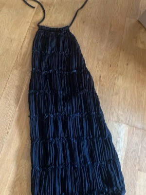 Svart  kortklänning med snörning - Säljer en svart kortklänning med smockad struktur och tunna axelband som knyts i nacken. Klänningen har en snygg omlottkänsla och är perfekt för sommarens alla tillfällen. Materialet känns lätt och luftigt.
